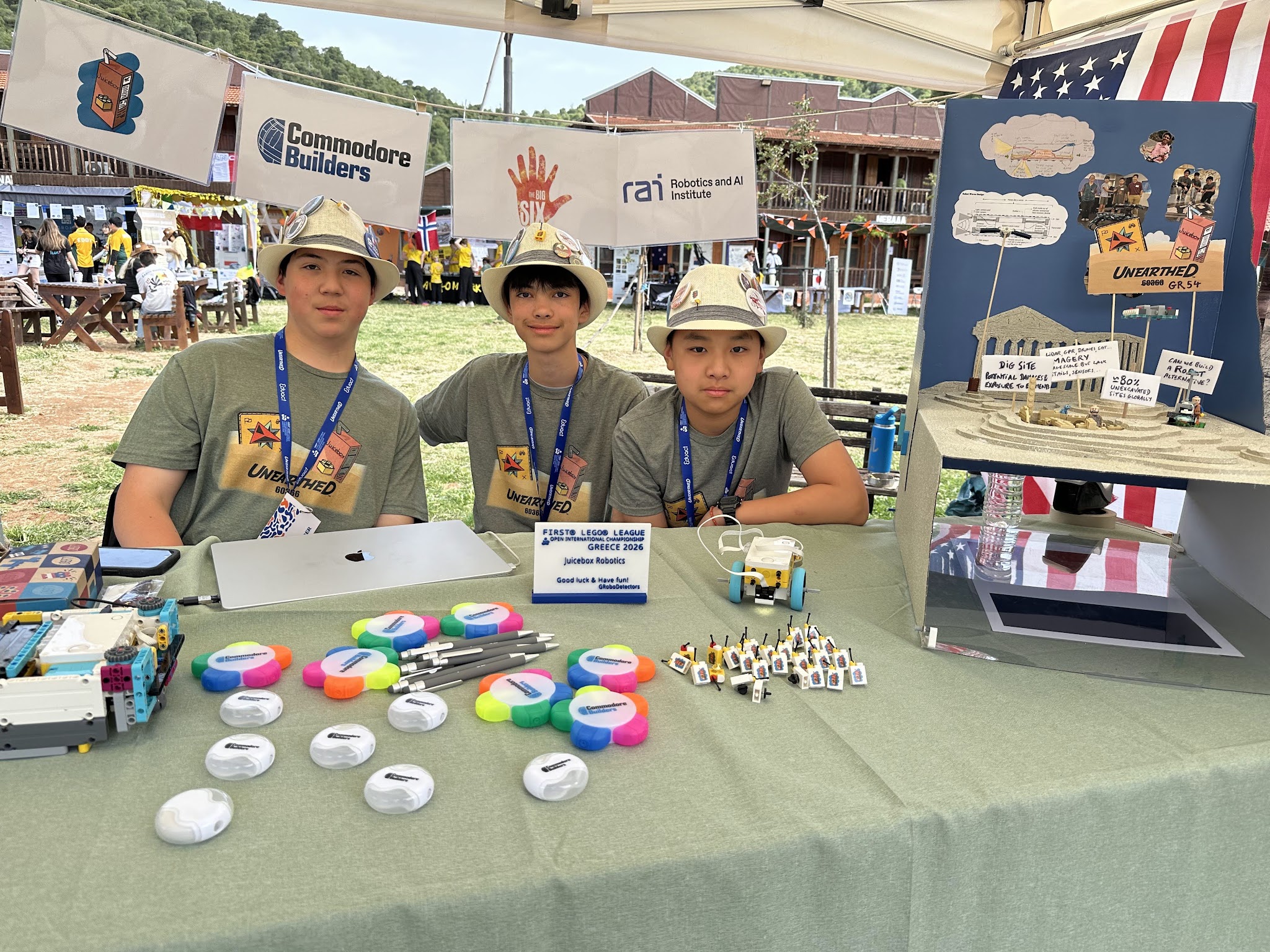 Three teammates at the Juicebox Robotics pit in Greece with prototypes and displays